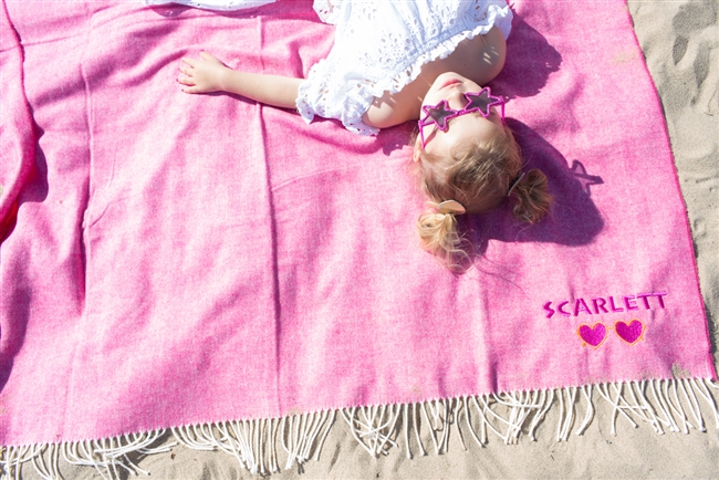 Wild pink blanket laying on the beach personalized with neon orange thread colors and heart sunglasses as the graphic.