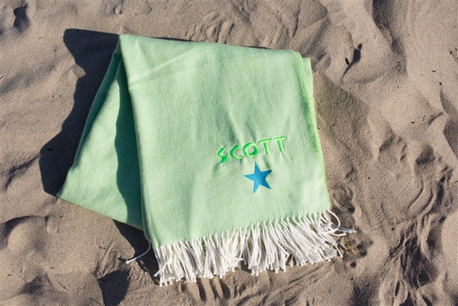 Lime Blanket laying on the beach personalized with neon green thread colors and a neon blue star graphic.