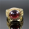 Sultry Sovereign Ring photo. This is a very royal design, The 18k yellow gold really combines well with the round, center red rhodolite creating a Sultry Sovereign. The details are little dots and braided designs on the sides.