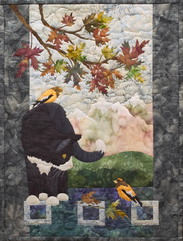 Quilt block of a black cat with white nose, paws, and chest under an Autumnal maple branch looking at a bird, while another bird sits on his back