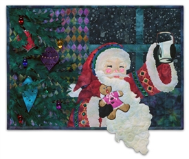 Quilt block of Santa in front of a decorated tree, raising a glass to the kind person that left him cookies and milk.
