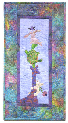 Quilt block of a giraffe holding up a turtle, a bunny, and a teddy bear, with a little bird flying above them