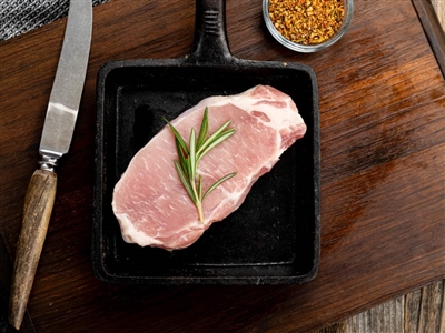 Two pork loins grilling alongside fresh corn