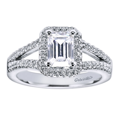 An emerald cut center diamond is shown off in the middle of this contemporary halo engagement ring available in white gold or platinum.