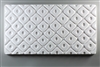 A long rectangular tile made of white ceramic. The carved texture is filled with a repeating pattern of diamonds. The diamonds are raised while the lines between them are carved. Each diamond has a small oval carved in its middle.