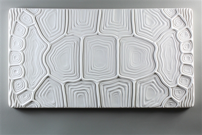 A long rectangular tile made of white ceramic. The carved texture has the appearance of a tortoise shell that has been flattened to occupy the space. The shell design takes up the entire tile.