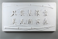 A long rectangular tile made of white ceramic. The carved texture has Chinese characters in the middle with two stalks of bamboo bordering them, one above and one below. The text roughly translates to beauty is everywhere as long as you look for it.