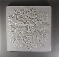 A large square tile made of white ceramic. The carved texture has the details of a manâ€™s face in the center emerging from a cluster of leaves and other foliage.