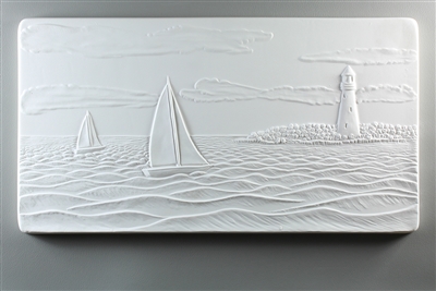 A long rectangular tile made of white ceramic. The carved texture shows a seascape with two sailboats on the waves. There is a peninsula to their right with a lighthouse, and the sky above them has a few long, wispy clouds.