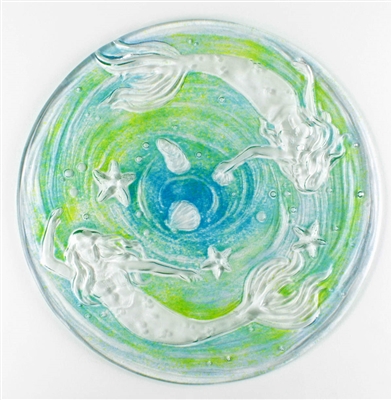 A top-down view of a clear glass dish with a mermaid design. The glass is clear. The two mermaids swimming around the edges of the dish are also clear, but the space between them has been filled with a swirl of teal and light green.