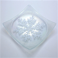 A clear glass dish. The dish is a square with a snowflake design embossed into a circle in the center. The snowflake is filled with white.