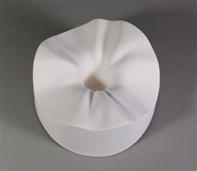 A circular white ceramic mold for fusing glass on a grey background. It is carved into a ruffled and waved shape around its outside, which drops quickly and deeply down into a small circle in the center.