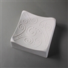 A square white ceramic mold for fusing glass on a grey background. Each corner of the square curves slightly upwards. The mold has been carved with several swirling lines and small dot accents.