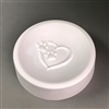 A tall circular white ceramic mold for fusing glass on a grey background. The edges are raised into a small border like a dish, and the bottom has been carved with a heart shape with two small pawprints in its top left.