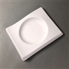 A rectangular white ceramic mold for fusing glass on a grey background. There is a circle in the center carved gently inwards like a shallow dish. The rectangular portion of the mold has a slight s-curve shape to it, with the middle being slightly higher.