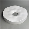 A large flat circular white ceramic mold for fusing glass on a grey background. A small circle has been cut through the very center, and the surrounding ring slopes gently downwards into the empty space. The ring has a gentle overall wave shape to it.