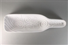 A bottle-shaped white ceramic mold for fusing glass on a grey background. The outer edges curve upwards, giving the mold a bowl-like shape. The mold has been carved many spiraling lines across its entirety.