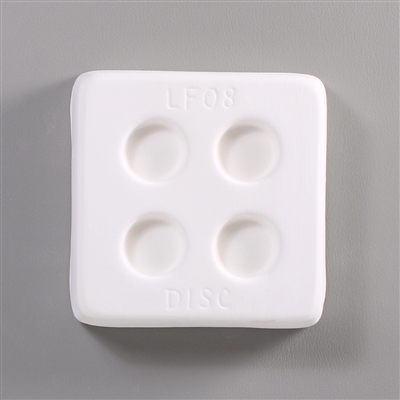 A square, white ceramic mold for fusing hot glass on a grey background. Four small circles, evenly spaced apart, have been carved into it. The mold has LF08 Disc engraved on the sides in print.