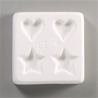 A square, white ceramic mold for fusing hot glass on a grey background. Two small hearts and two small stars, evenly spaced apart, have been carved into it, with the hearts at the top and stars at the bottom. The mold has LF09 engraved in the middle.