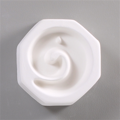 An octagonal, white ceramic mold for fusing hot glass on a grey background. A simple counterclockwise spiral has been carved into it. There is a small post at the top of the spiral so the finished piece can be strung as jewelry.