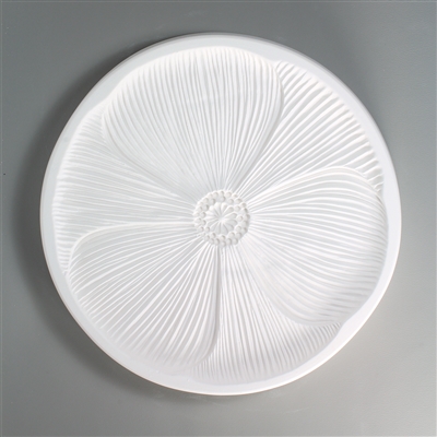 A round, white ceramic mold for fusing hot glass on a grey background. A large flat detailed poppy flower has been carved into it and occupies most of the surface of the mold.  There is thin ring of empty space around the outside of the flower.