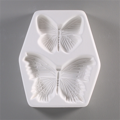 A roughly hexagonal, white ceramic mold for fusing hot glass on a grey background. Two small, detailed butterflies have been carved into it. The top butterfly is smaller with only lines on the wings. The bottom is larger with lined and dotted wings.