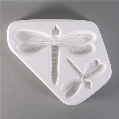 A white ceramic mold for fusing hot glass on a grey background. The mold is somewhat triangular and has two detailed dragonflies carved into it. The larger dragonfly faces upward and the smaller dragonfly to its lower right faces the lower right corner.