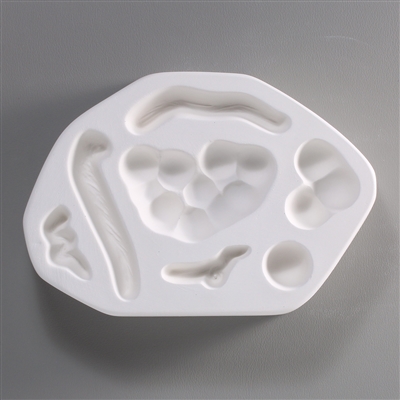A roughly oval, white ceramic mold for fusing hot glass on a grey background. Two separate bunches of grapes, a single grape, and four shapes of thin twisting vine have been carved into it. Each shape is separate.