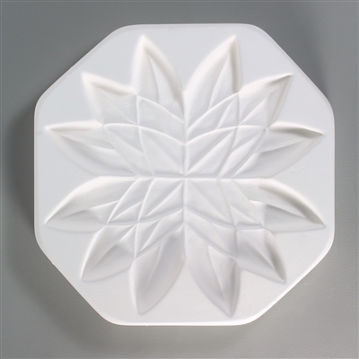 An octagonal, white ceramic mold for fusing hot glass on a grey background. A stylized, highly symmetrical, flat lotus flower has been carved into it.