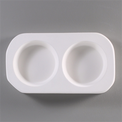 A roughly rectangular, white ceramic mold for fusing hot glass on a grey background. Two simple and identical circles have been carved into it.