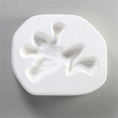 A roughly circular, white ceramic mold for fusing hot glass on a grey background. A top-down view of a frog has been carved into it. The frog is facing left with outstretched arms and legs. The mold has Little Fritters #13 engraved on the bottom in script