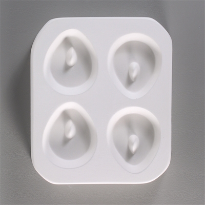 A rectangular, white ceramic mold for fusing hot glass on a grey background. Four small, rounded tear shapes have been carved into it with equal distance between them. Each tear has a post towards its top to allow for stringing into jewelry after firing.