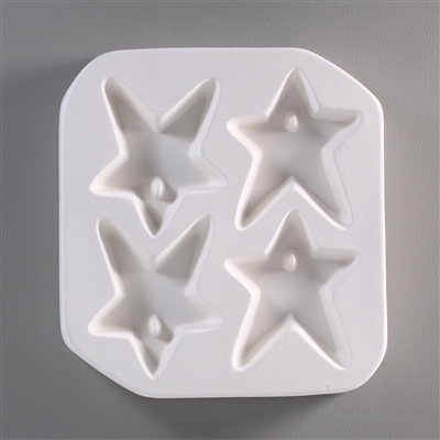 A square, white ceramic mold for fusing hot glass on a grey background. Four five-pointed stars have been carved into it with equal distance between them. Each star has a post in its top to allow for stringing into jewelry after firing.