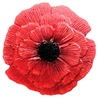 A bright red fused glass poppy flower on a transparent background. The petals are textured with many small lines. The center is black, and there are a few black speckles throughout the petals.