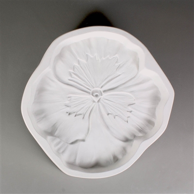 A circular, white ceramic mold for fusing hot glass on a grey background. A realistic flat pansy flower has been carved into it. The flower takes up most of the mold, but there is a small border of empty space around it.