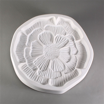 A circular, white ceramic mold for fusing hot glass on a grey background. A small, intricately detailed flat poppy flower has been carved into it. The flower takes up most of the mold, but there is a small border of empty space around it.