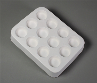 A rectangular white ceramic mold for fusing hot glass on a grey background. Twelve identical small circles have been carved into it with equal spacing between them.