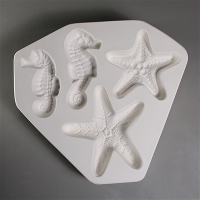 A roughly triangular white ceramic mold for fusing hot glass on a grey background. Two seahorses and two starfish have been carved into it. Each animal has a slightly different design than its counterpart, but all are similarly sized.