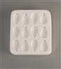 A square white ceramic mold for fusing hot glass on a grey background. Twelve identical tears have been carved into it with equal space between them, though half are facing the opposite direction.