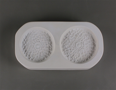 A rectangular white ceramic mold for fusing hot glass on a grey background. Two detailed flat zinnia flowers have been carved into it. The one on the right is slightly larger.