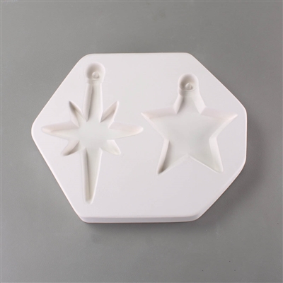 A roughly hexagonal white ceramic mold for fusing hot glass on a grey background. Two different stars with ornament caps have been carved into it. The right star has five points, the left eight. The ornament caps have posts in the middle to hang from.