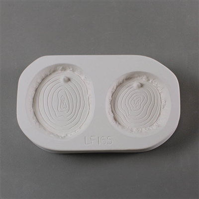 A rectangular white ceramic mold for fusing hot glass on a grey background. Two flat circular log slices have been carved into it, each showing age ring details. The left slice is slightly larger. Each slice has a post at the top to hang from.