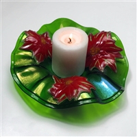 A ruffled green fused glass bowl holding a candle on a light grey background. The green is slightly iridescent, and three bright red glass poinsettias are spaced equally around the bowl as decoration. The candle is white and lit.