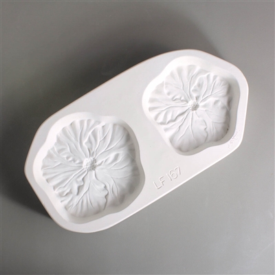 A rectangular white ceramic mold for fusing hot glass on a grey background. Two flat detailed hibiscus flowers have been carved into it. The left flower is slightly larger but both flowers have similar designs.