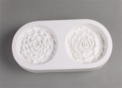 An oval-shaped white ceramic mold for fusing hot glass on a grey background. Two detailed round flat succulents have been carved into it. The right succulent is slightly larger, and has fewer but wider petals than the left.