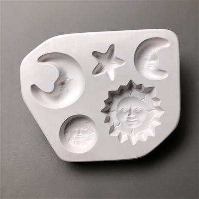 A trapezoidal white ceramic mold for fusing hot glass on a grey background. Five celestial objects have been carved into it. There are two crescent moons, a large sun with pointed rays, a small circular sun, and a star. The moons and suns all have faces.