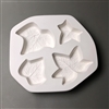 A circular white ceramic mold for fusing hot glass on a grey background. Four ivy leaves have been carved into it. Each leaf is shaped and sized slightly differently, with two having three points and two having five.