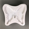 A large white ceramic mold for fusing hot glass on a grey background. A large and intricately detailed butterfly has been carved into it.