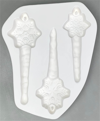 A roughly triangular white ceramic mold for fusing hot glass on a grey background. Three separate sizes and designs of snowflakes all on top of icicles have been carved into it. Each snowflake has a post at the top to allow for hanging after firing.