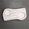 A long white ceramic mold for fusing hot glass on a grey background. Two stylized daisies with smiles in the centers and stems turning into stakes have been carved into it. They are facing opposite directions and the top stake is slightly smaller.